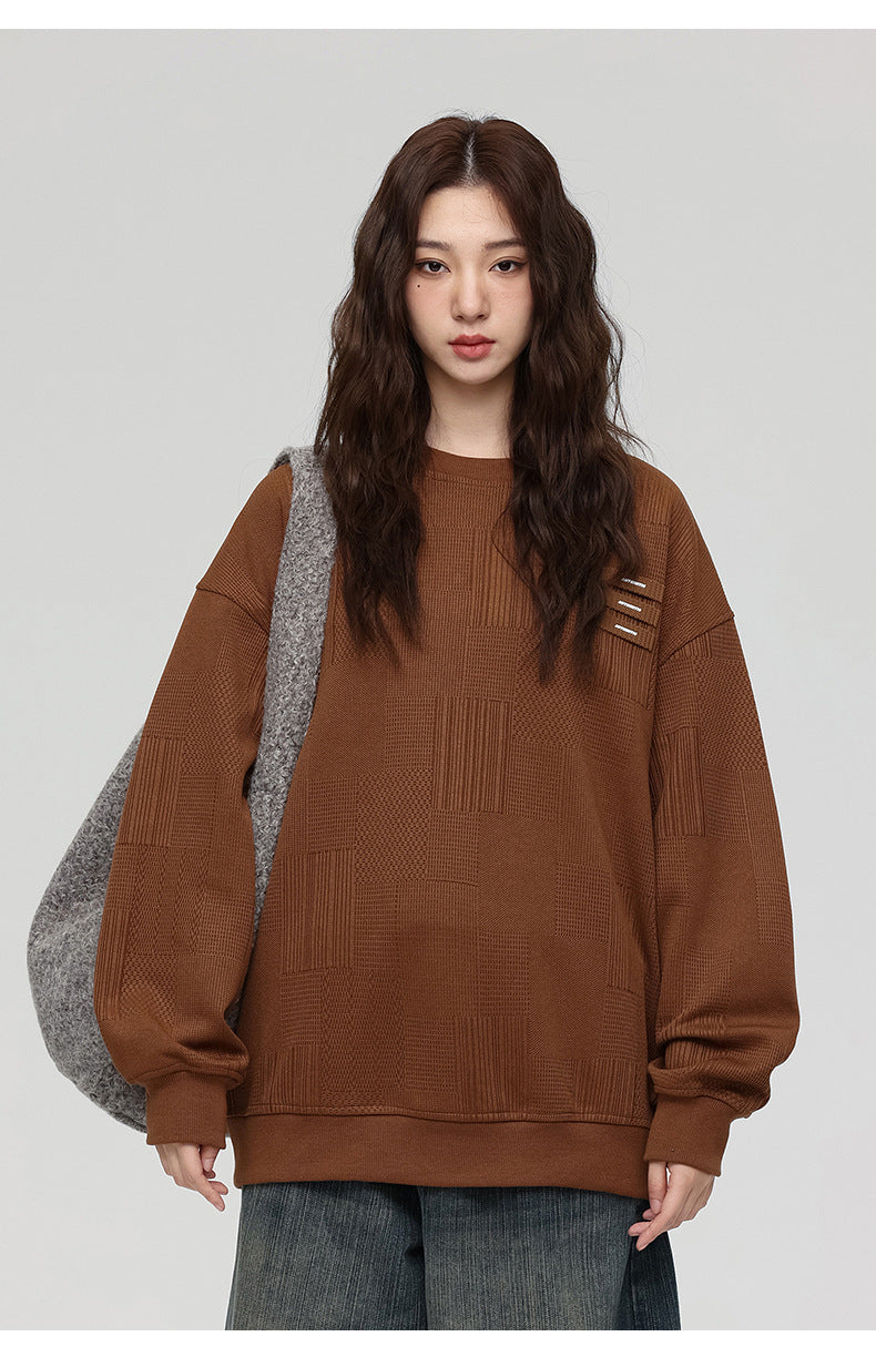 Close-up of woman with wavy brown hair wearing brown textured sweatshirt with three decorative tabs