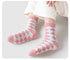 Pink and white argyle patterned fuzzy socks worn with white sweater