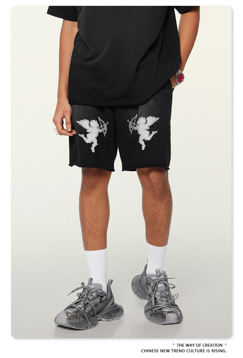 Close-up of black cotton shorts with white cupid angel graphics, shown with white socks and gray chunky sneakers