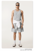 Model in gray tank top and shorts with a white sweatshirt tied around the waist, wearing sunglasses and accessories
