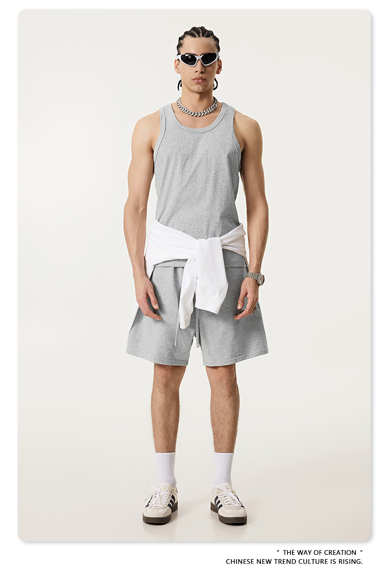 Model in gray tank top and shorts with a white sweatshirt tied around the waist, wearing sunglasses and accessories