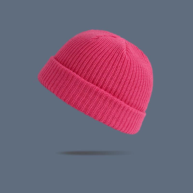 A bright pink ribbed knit beanie with folded cuff floating against slate gray background, showing vibrant winter hat style