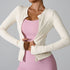 A model is adjusting a cream zip-up workout jacket showing pink sports bra underneath. Athletic fit with streamlined silhouette and minimalist design