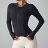 A model is wearing a black performance jacket with technical seaming and front zip closure. Hands positioned at waistband of cream leggings