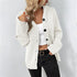 White knit cardigan with black buttons, layered over a white crop top and black jeans, accessorized with a gold belt and pendant necklace