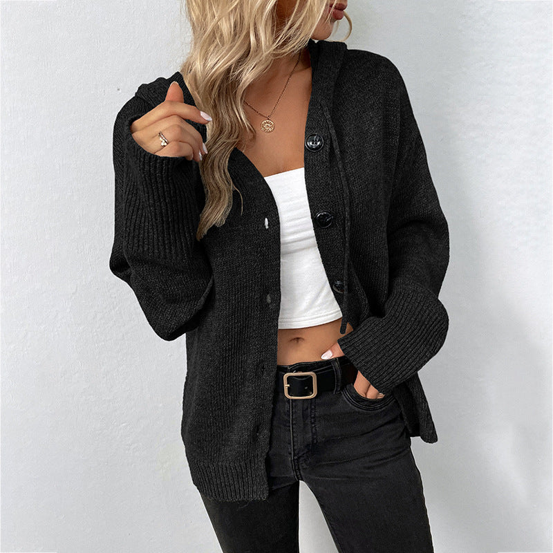 Black knit cardigan with large buttons, worn over a white crop top and black jeans, styled with a gold belt and delicate necklace