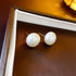 White 12mm pearl stud earrings displayed on white and dark brown frame, showing lustrous finish