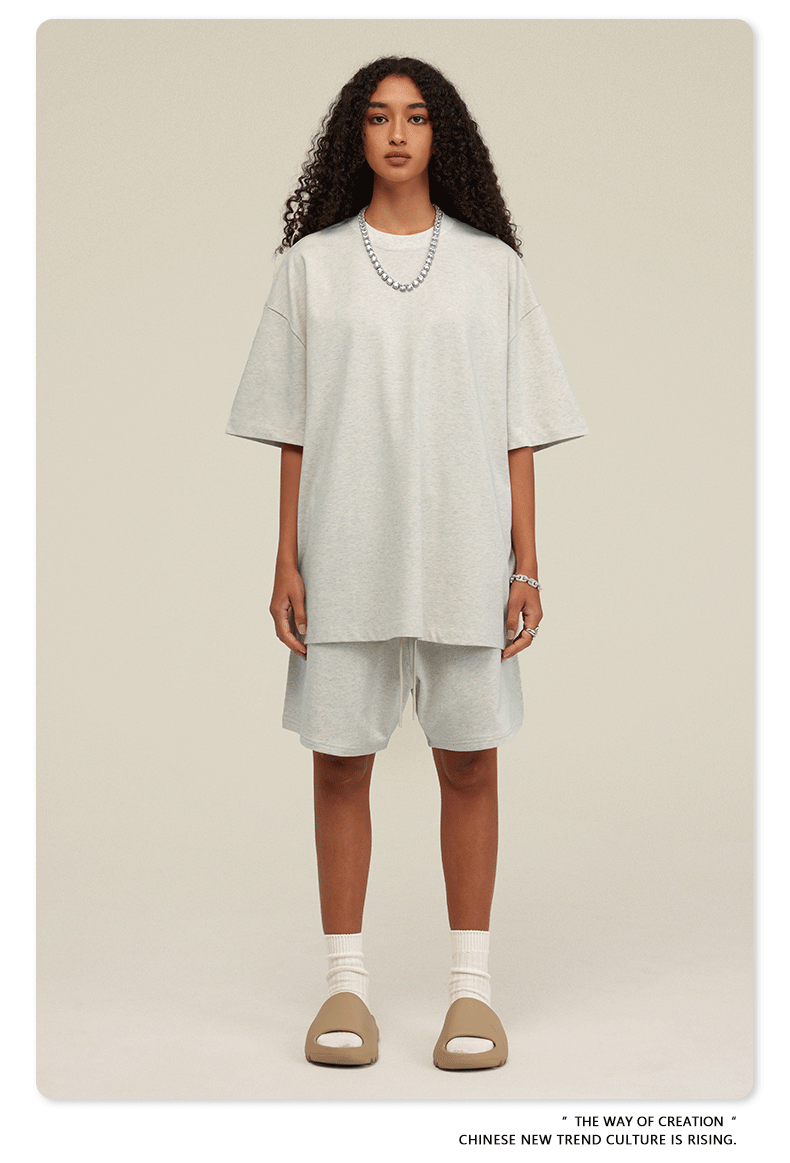 Woman with curly hair modeling white oversized T-shirt and shorts set with beige slide sandals