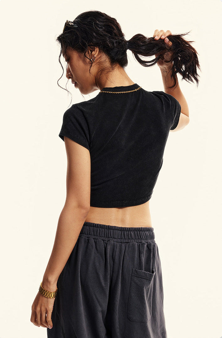 Model holds her ponytail, showing the back of a fitted black cropped T-shirt and loose dark sweatpants