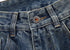 Close-up of denim waistband showing metal button closure and belt loop detail with visible fabric texture