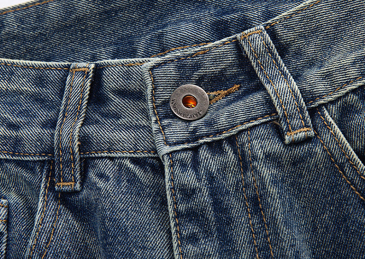 Close-up of denim waistband showing metal button closure and belt loop detail with visible fabric texture