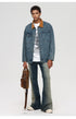 Man wearing denim jacket with brown corduroy collar over white graphic tee and light wash jeans holding brown bag