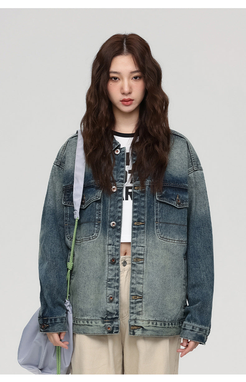 A woman is standing directly facing camera against gray background. Wearing oversized faded denim jacket, white graphic tee and carrying gray shoulder bag