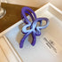 A deep purple butterfly-shaped hair claw with a gradient fade, placed in a beige jewelry case.