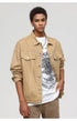 A man wearing tan denim jacket with chest pockets poses in white graphic tee with silver chain