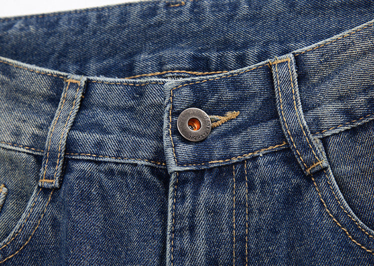 Close-up details of denim jeans showing brass YKK zipper hardware with contrasting stitching on dark indigo fabric above