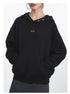 Front view of black oversized hoodie highlighting snap-button collar detail, eye logo placement, and relaxed fit silhouette