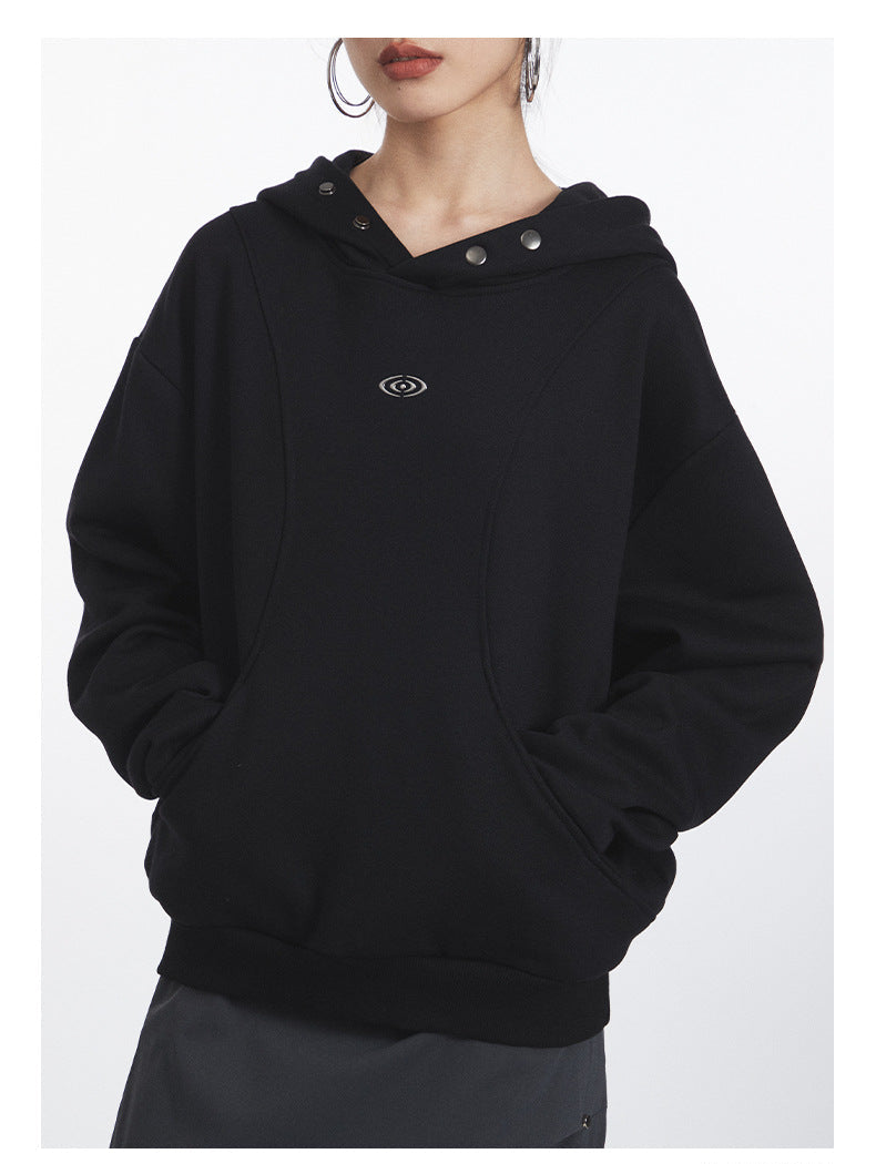 Front view of black oversized hoodie highlighting snap-button collar detail, eye logo placement, and relaxed fit silhouette