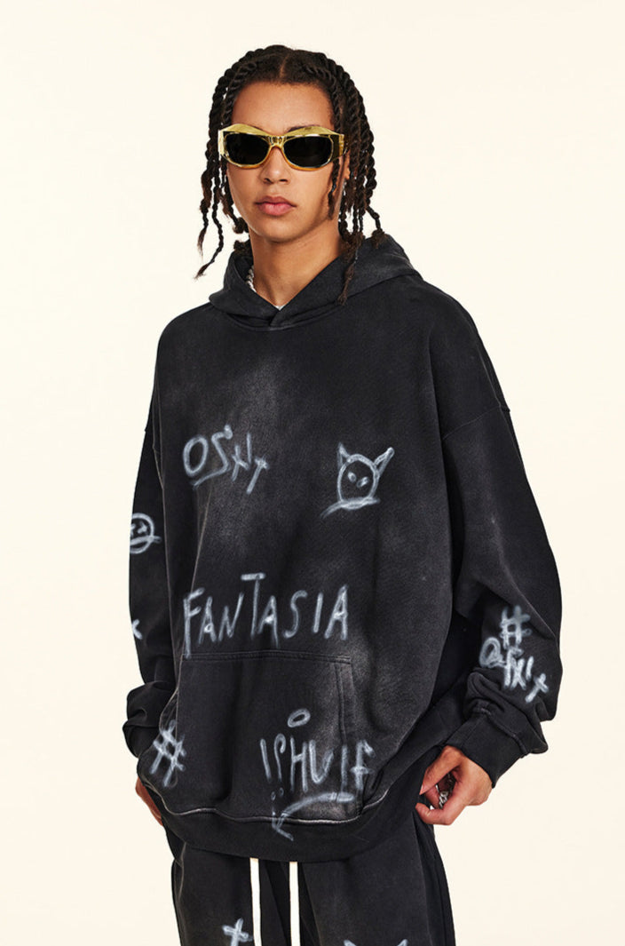 Close-up portrait of model wearing black graffiti hoodie with white painted designs and gold-framed sunglasse