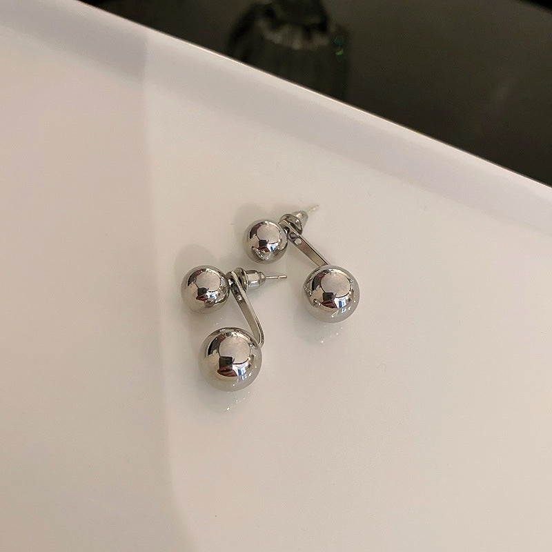 A pair of silver double-ball stud earrings with a reflective surface, displayed on a glossy white surface.