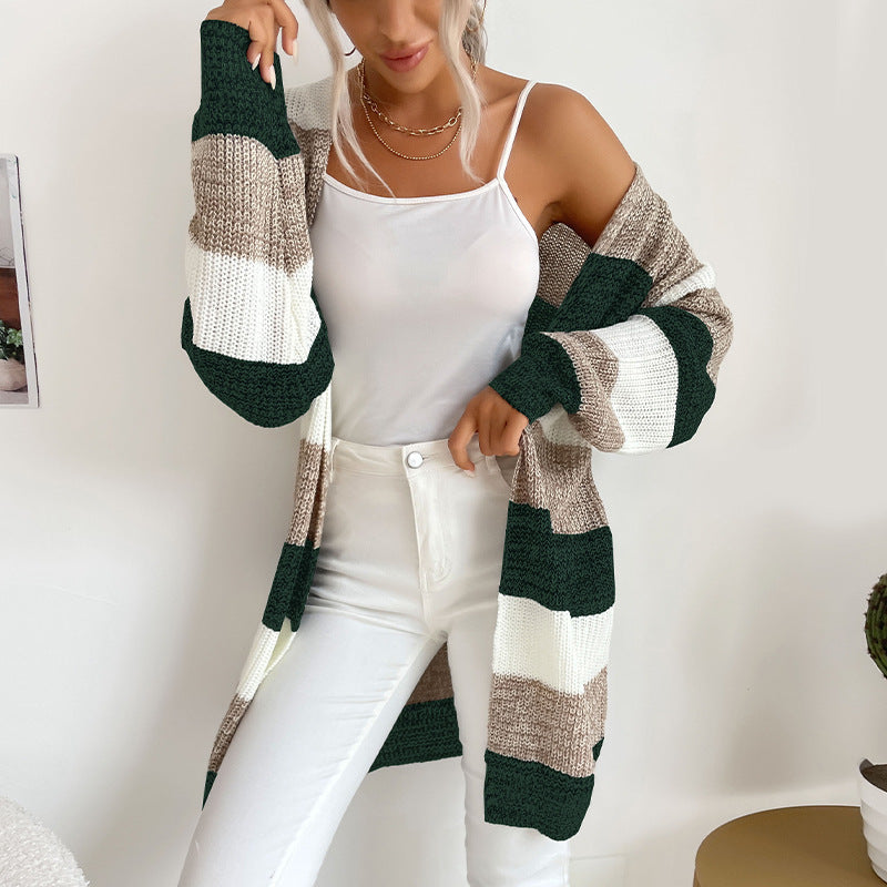 A woman modeling dark green, white and beige striped cardigan with white camisole and white jeans in minimalist home environment