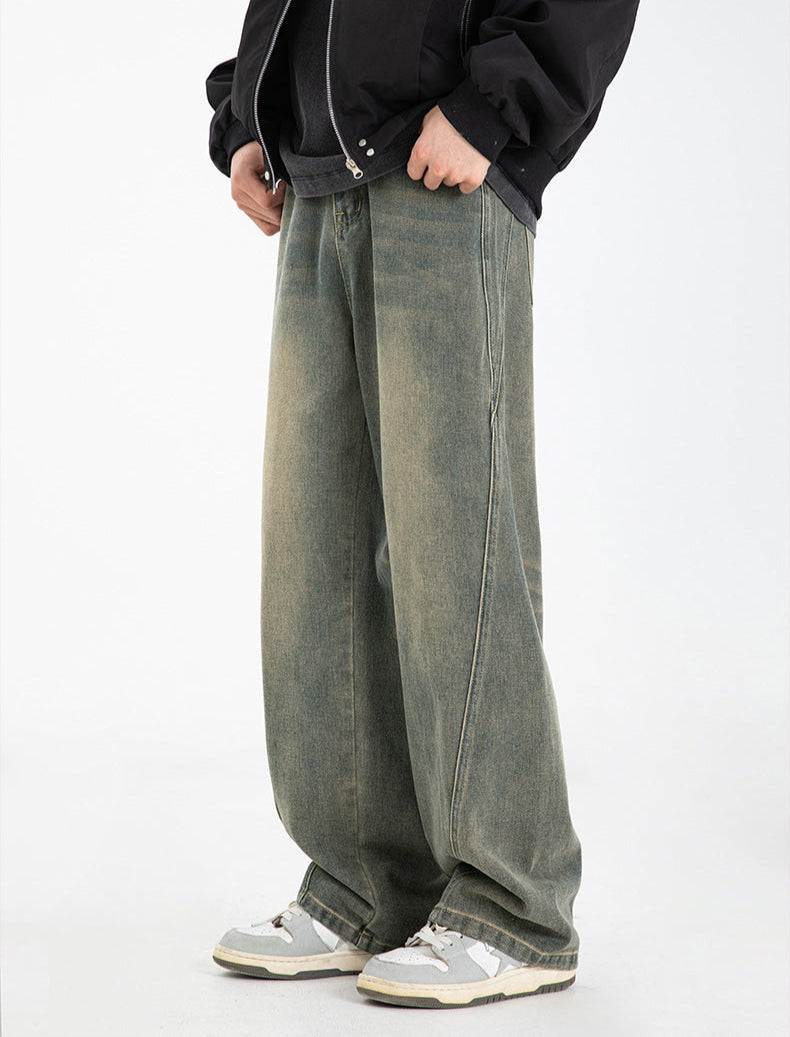 A model standing in olive-green wide-leg jeans with faded wash effect, black bomber jacket, hand in pocket, wearing gray and white athletic shoes