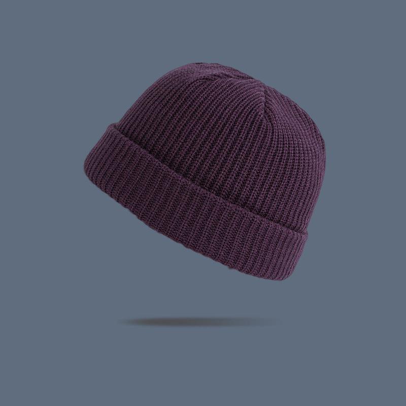 A plum purple ribbed knit beanie with folded cuff floating against slate gray background, displaying rich-colored winter hat