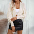 A woman wearing a cream cropped cardigan with sleeve ties over white bandeau top and black leather mini skirt against neutral wall