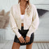 A woman modeling a white cable knit cropped cardigan with ribbon sleeve details paired with faux leather mini skirt and handbag