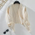 A cream cropped cardigan with cable knit pattern and tie sleeve details displayed on hanger against white background