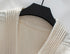 A close-up detail shot of cream cardigan neckline showing ribbed trim and textured knit pattern on black hanger