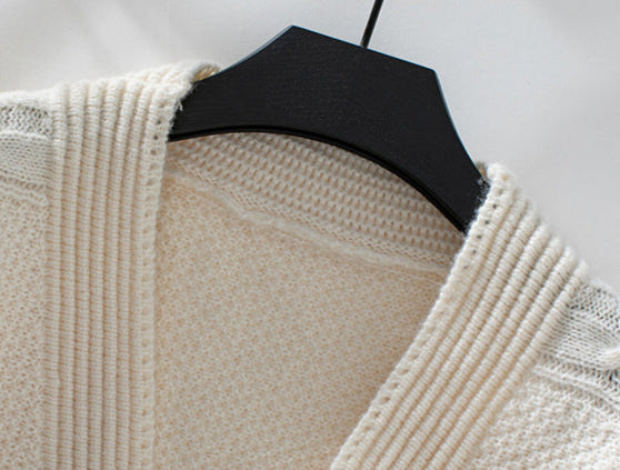 A close-up detail shot of cream cardigan neckline showing ribbed trim and textured knit pattern on black hanger