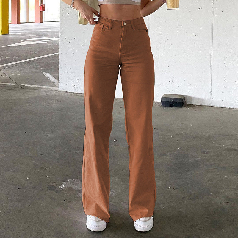 High-waisted terracotta straight-leg jeans with classic five-pocket design, shown with white sneakers against concrete wall