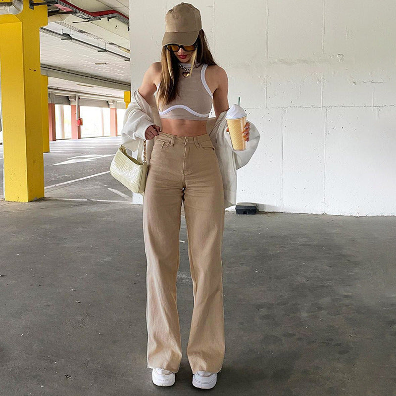 Full outfit view of beige straight-leg jeans styled with white sports bra, beige cap, and cream overshirt in parking structure