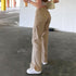 Side view of beige straight-leg jeans showing pocket placement and leg fit, paired with white sneakers in concrete setting
