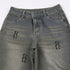 Close-up of gray baggy jeans showing embroidered gothic 'H' logo details on distressed denim fabric