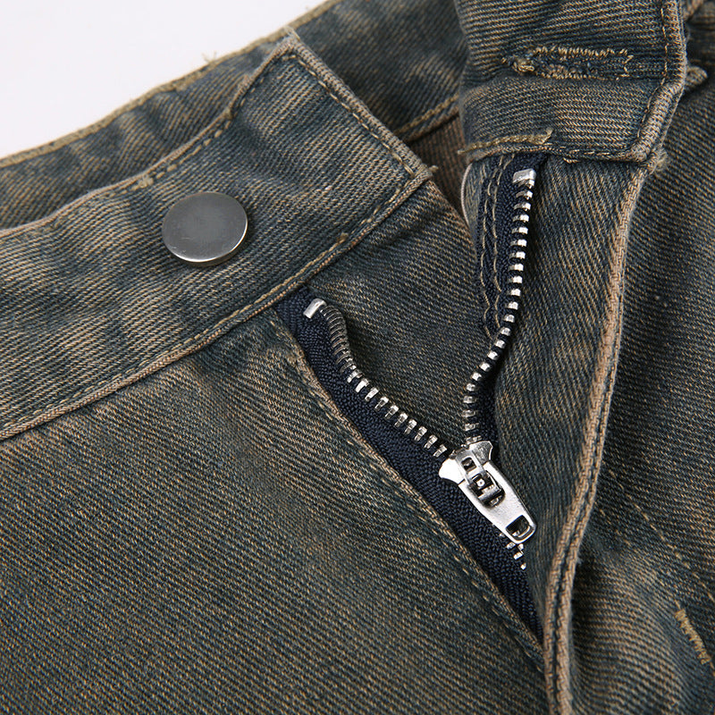 Close-up of gray jeans button closure and metal zipper detail on distressed denim