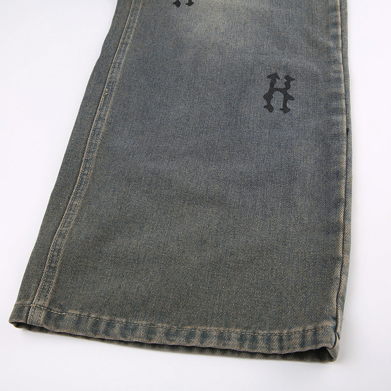 Side view of wide-leg gray jeans hem showing embroidered 'H' logo detail and distressed finish