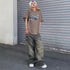 A woman wearing a brown graphic tee and baggy gray jeans poses against metal shutters, styled with white beanie and chunky sneakers