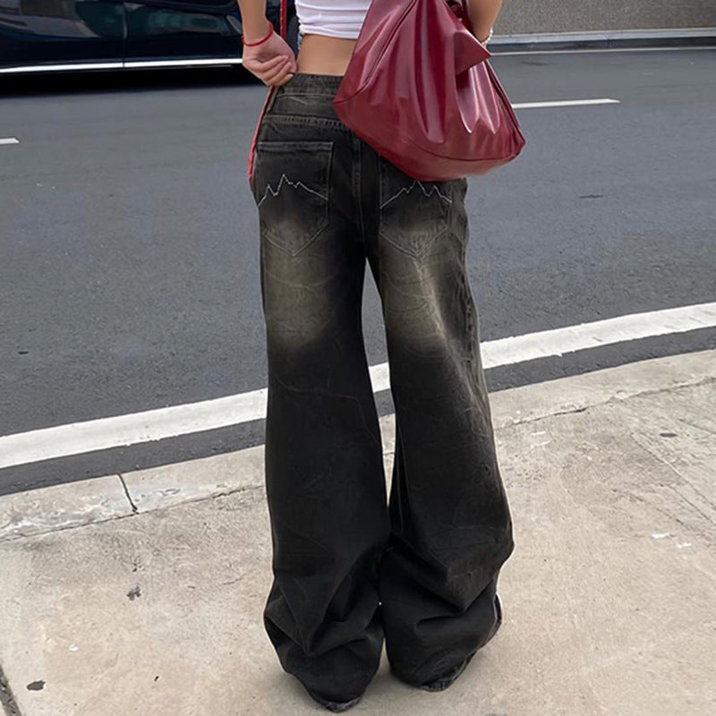 Rear view of black washed wide-leg jeans with subtle fading and embroidered back pockets, paired with a white crop top and red handbag