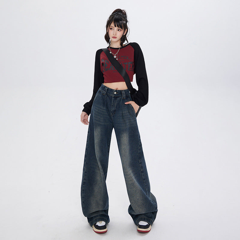 Model posing in oversized dark denim wide-leg jeans, burgundy crop top with black sleeves and platform sneakers on white background