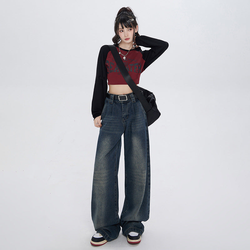 Model with updo hairstyle wearing cropped burgundy top with black sleeves, wide-leg dark denim jeans and black belt on white background
