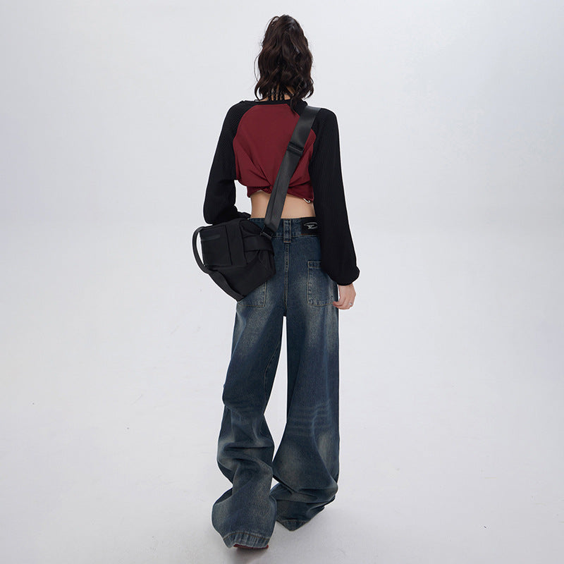 Back view of model wearing wide-leg denim jeans, burgundy and black crop top with crossbody bag against white backdrop