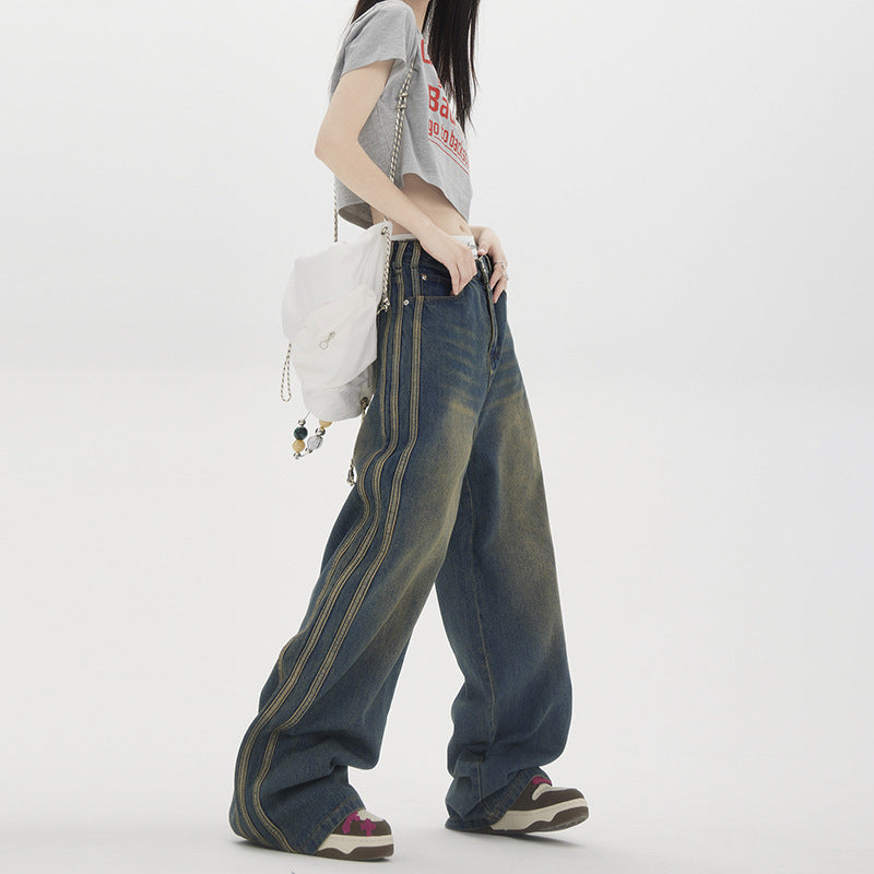 Side view of model in grey graphic crop top, wide-leg jeans with vertical stripe detail and white chain-strap bag against white backdrop