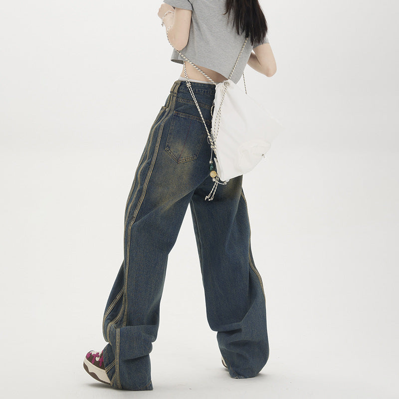 Back view of woman in grey crop top and oversized denim jeans with side stripes, carrying small white crossbody bag on white background