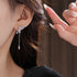 Close-up of crystal bow earring with dangling teardrop pendant, worn on ear with styled dark hair and neutral background