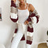 A woman wearing burgundy, beige and white striped long cardigan with white tank top and white pants against white wall