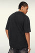A model shown from behind wearing a black oversized t-shirt. Displays cornrow braided hairstyle with silver chain visible at neckline