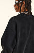 Close-up profile of model showing shoulder seam detail of black sweatshirt, twisted braids, white sunglasses, silver chain necklace visible