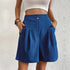 Model wearing blue pleated shorts with dual button closure and side pockets, paired with white crop top
